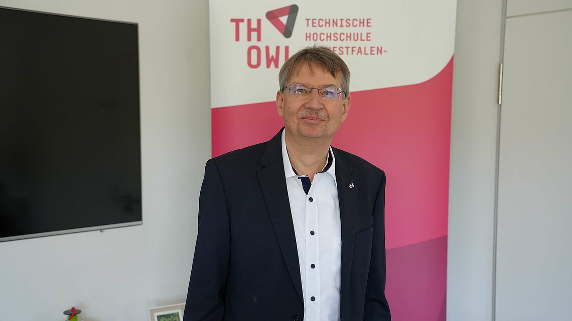 Sen-Prof. Dr. Volker Lohweg steht vor dem Logo der Technischen Hochschule Ostwestfalen-Lippe.